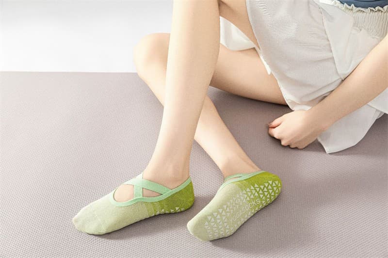 Green cross-strap Pilates grip socks worn during studio movement