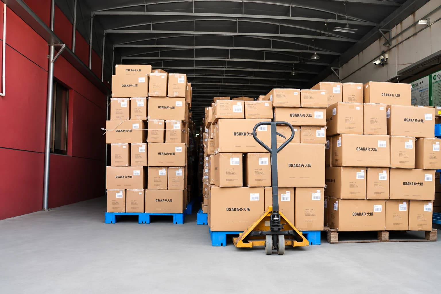 Sock order cartons stacked on blue pallets beside a pallet jack at the warehouse entrance