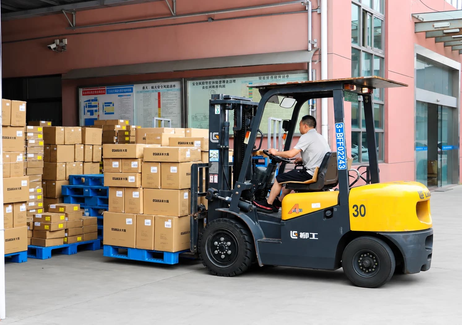Forklift operator moving palletized cartons at the factory loading area