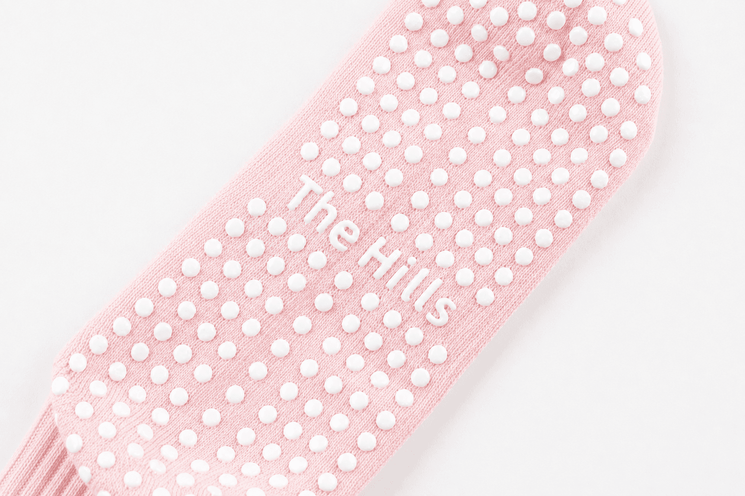 Custom silicone studio logo integrated into the grip pattern of a pink Pilates sock