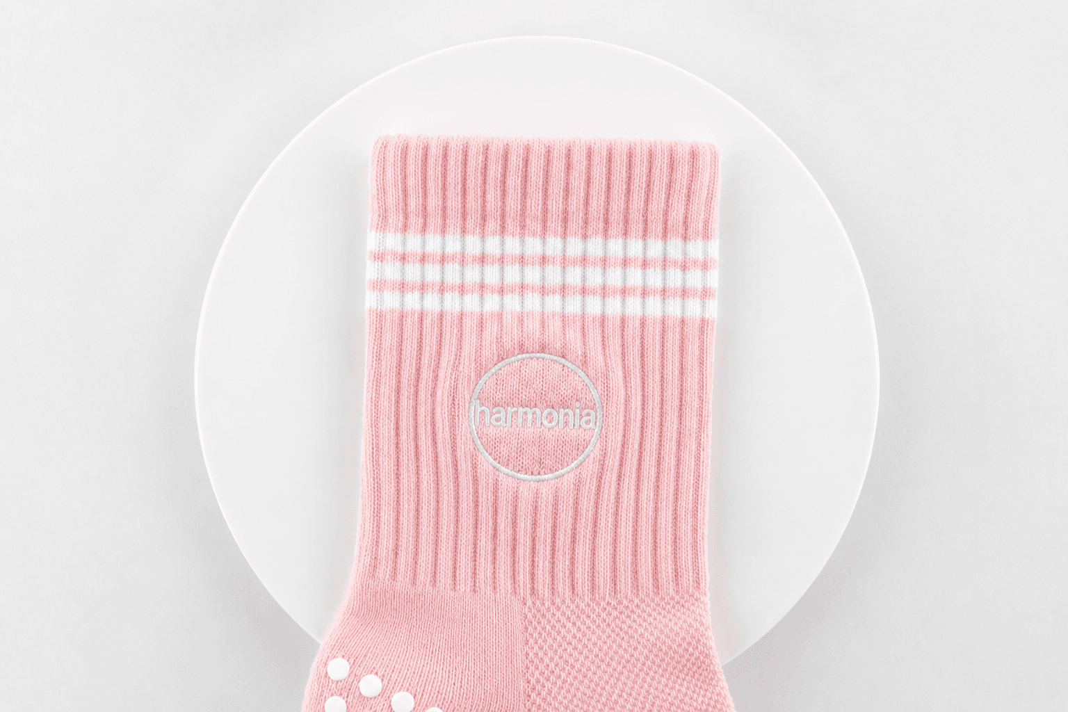 Front view of a pink Pilates sock with embroidered studio logo and contrast stripes