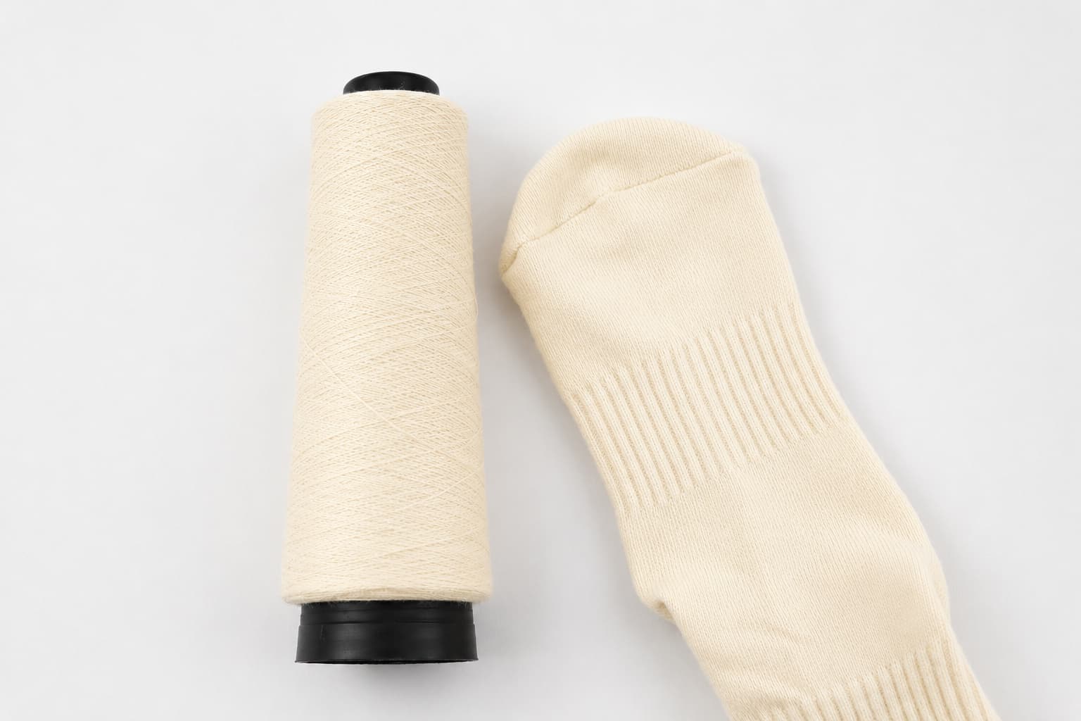 Cream sock yarn cone beside a knitted Pilates sock sample